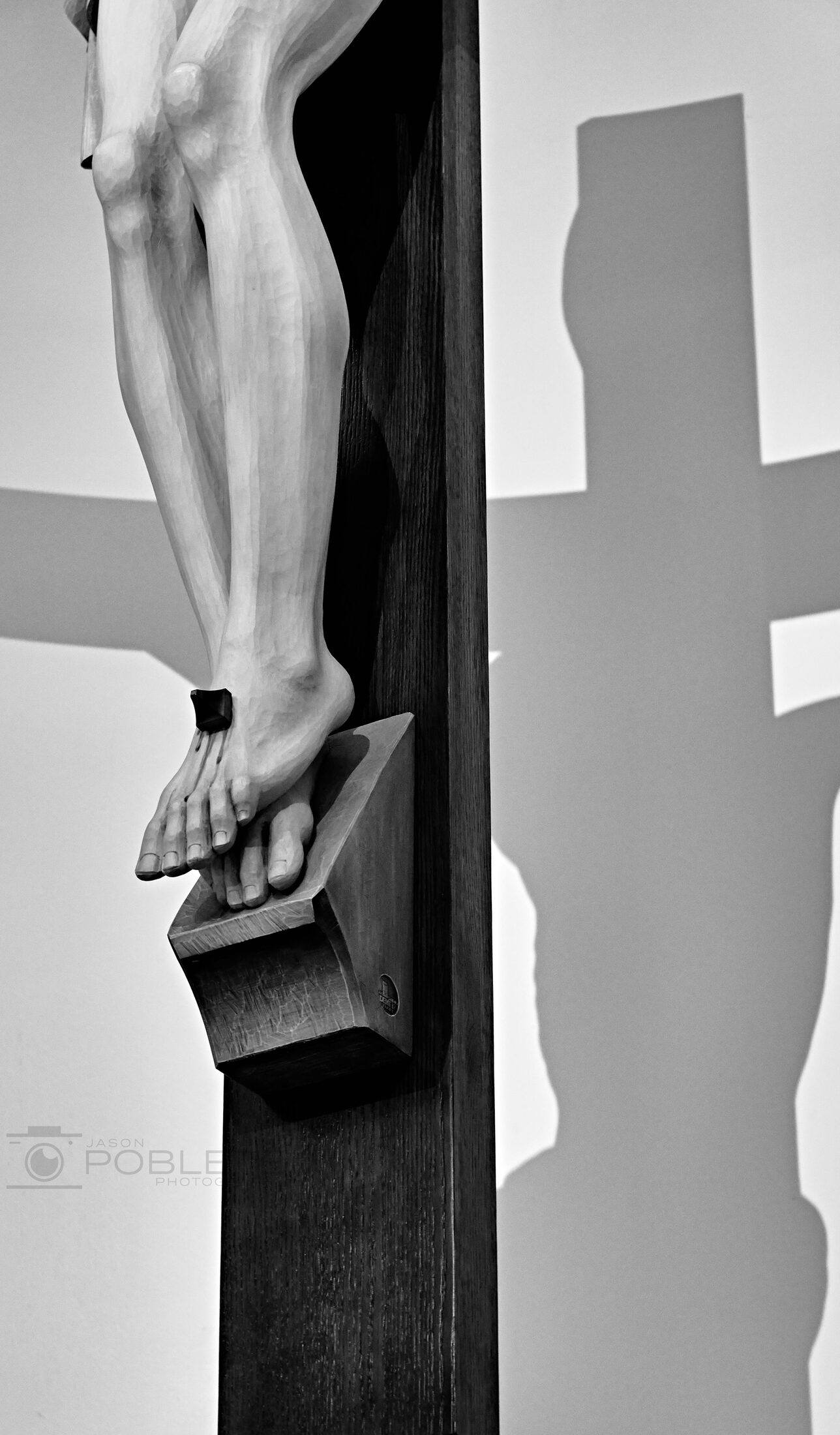 A narrow view of a robed statue casting a strong shadow on a wall.