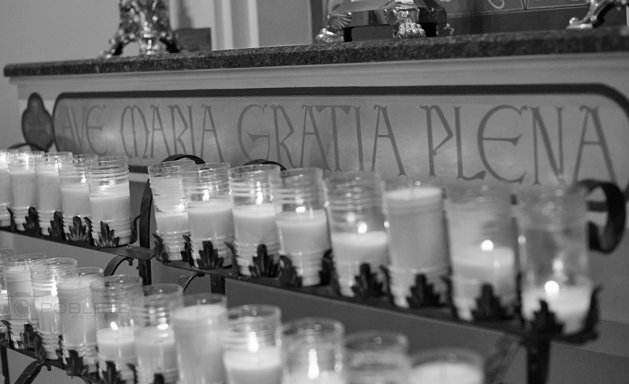 Rows of votive candles burn beneath an inscribed stone wall.