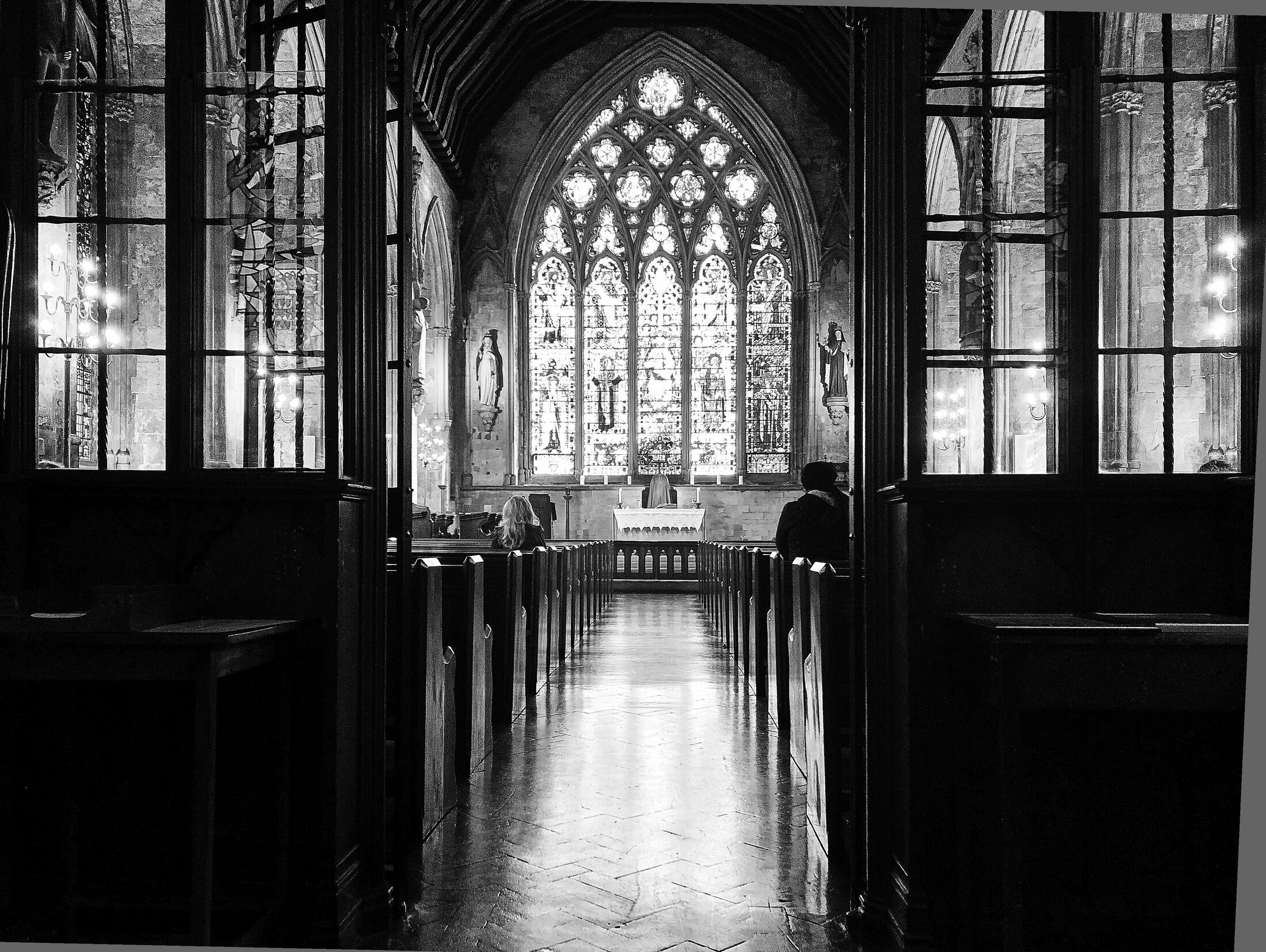 An empty church aisle leads toward a bright stained-glass window.