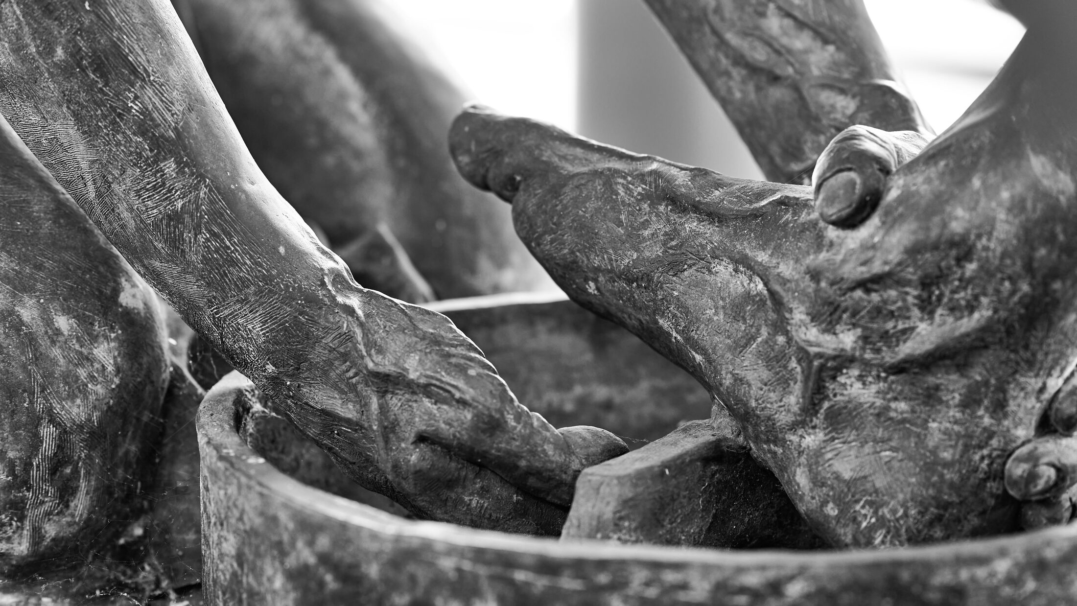 Sculpted hands hold a foot above the rim of a basin.