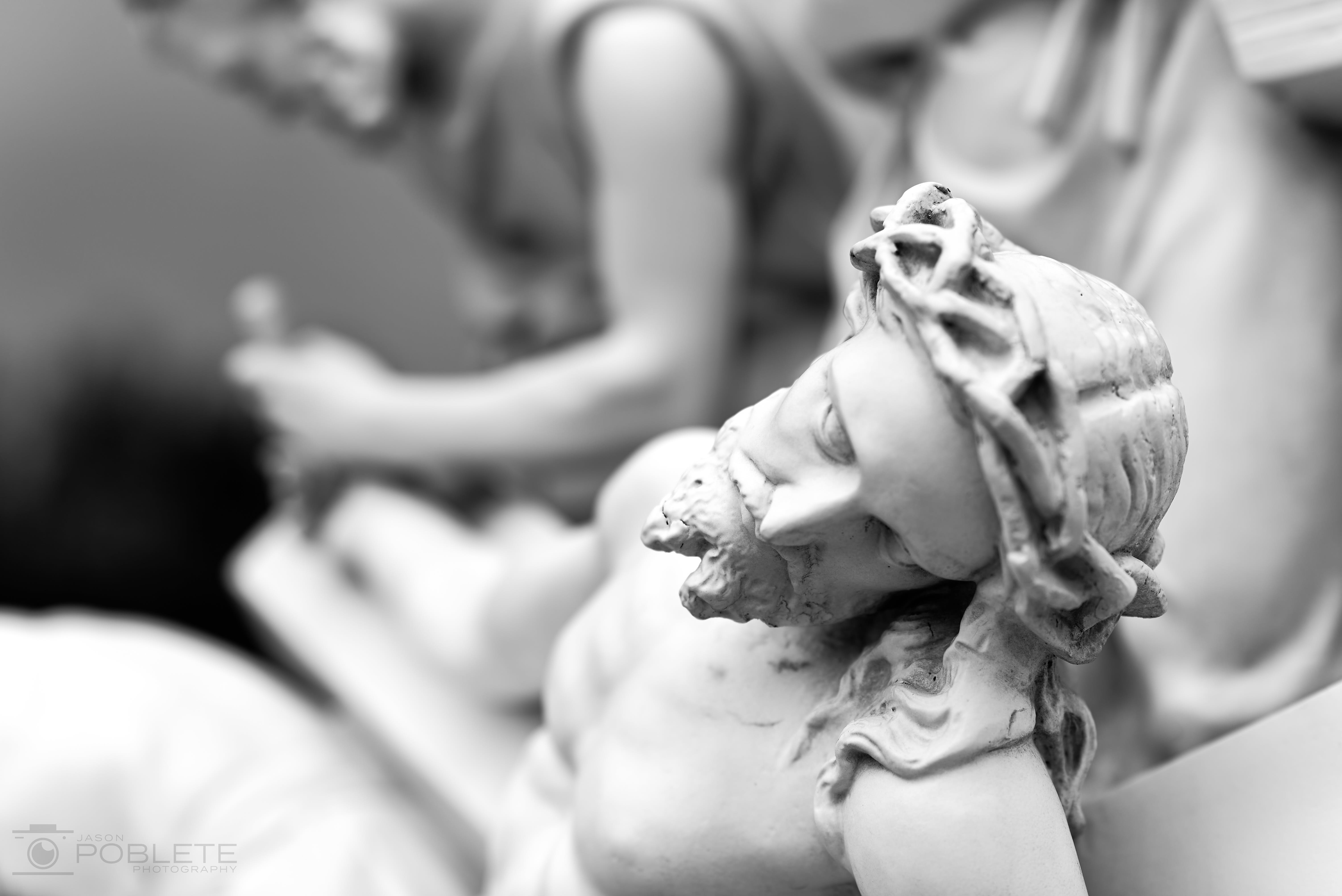 A close view of a carved religious figure wearing a crown of thorns, with another figure blurred behind.