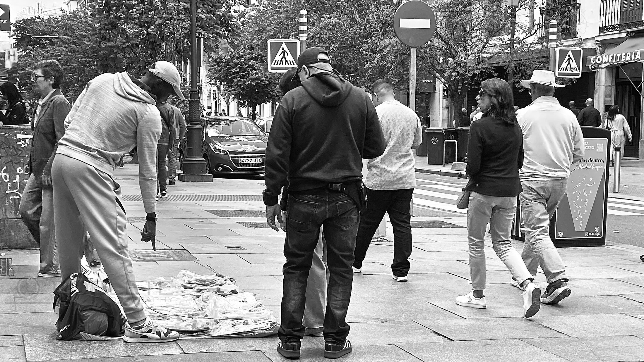 Workers and pedestrians gather around goods spread across a city sidewalk.