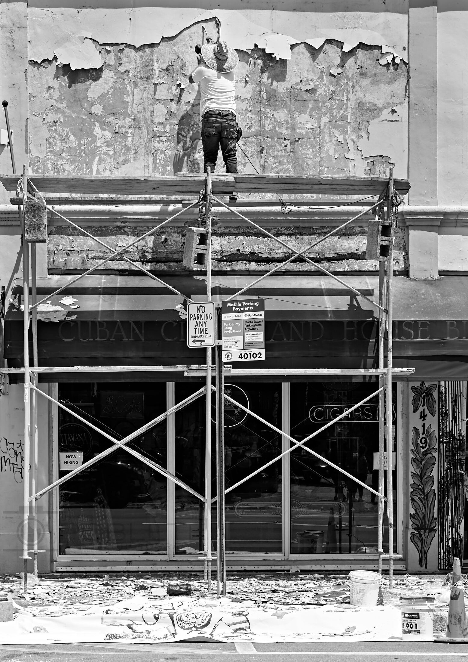 A construction worker stands high on scaffolding against a damaged wall.