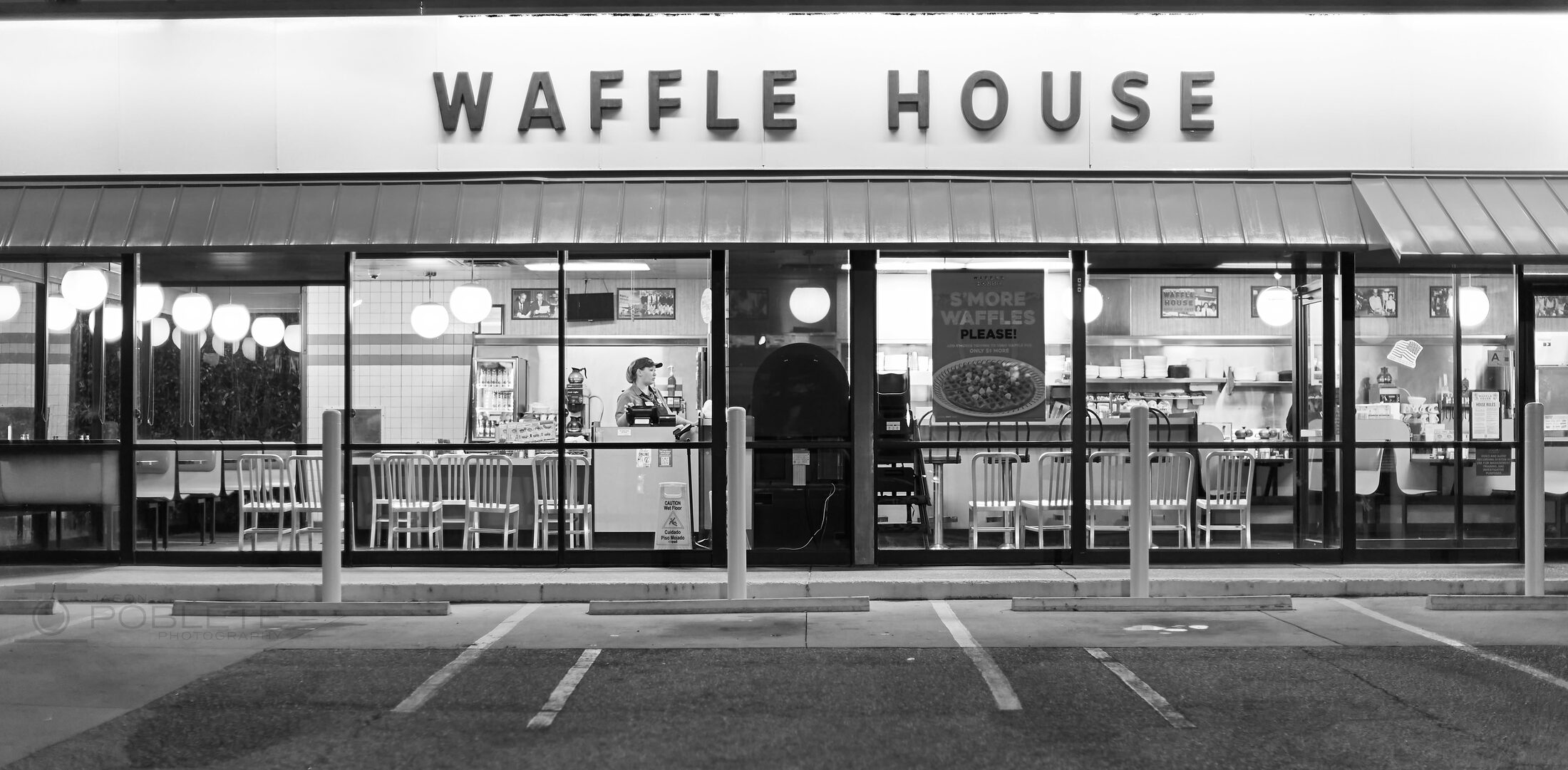 A worker stands inside a brightly lit Waffle House at night.