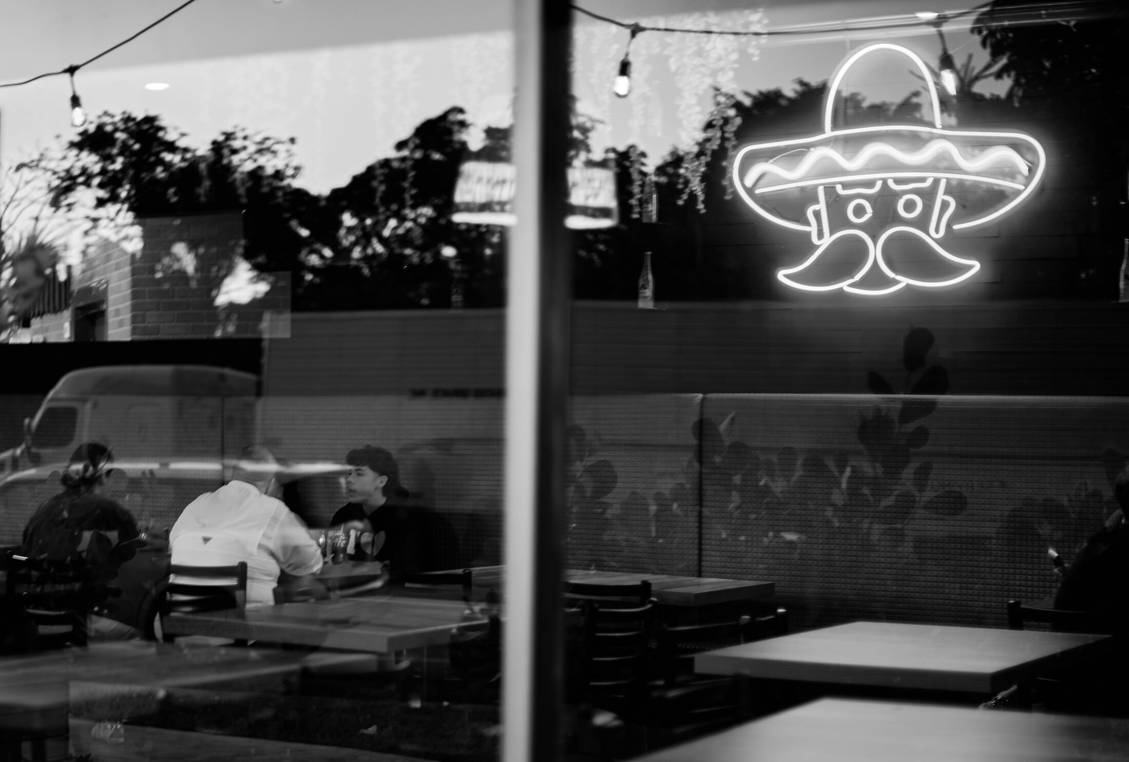 An empty restaurant booth is reflected beneath a glowing neon sign.