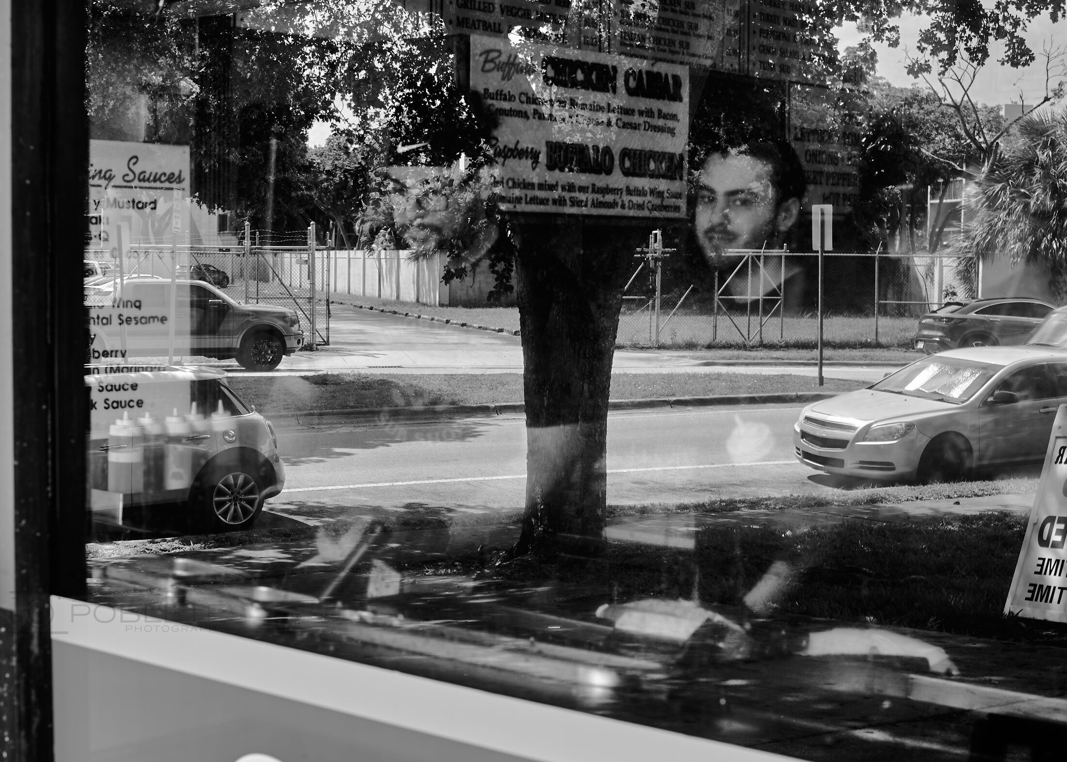 A man stands behind a shop window layered with reflections of passing traffic.
