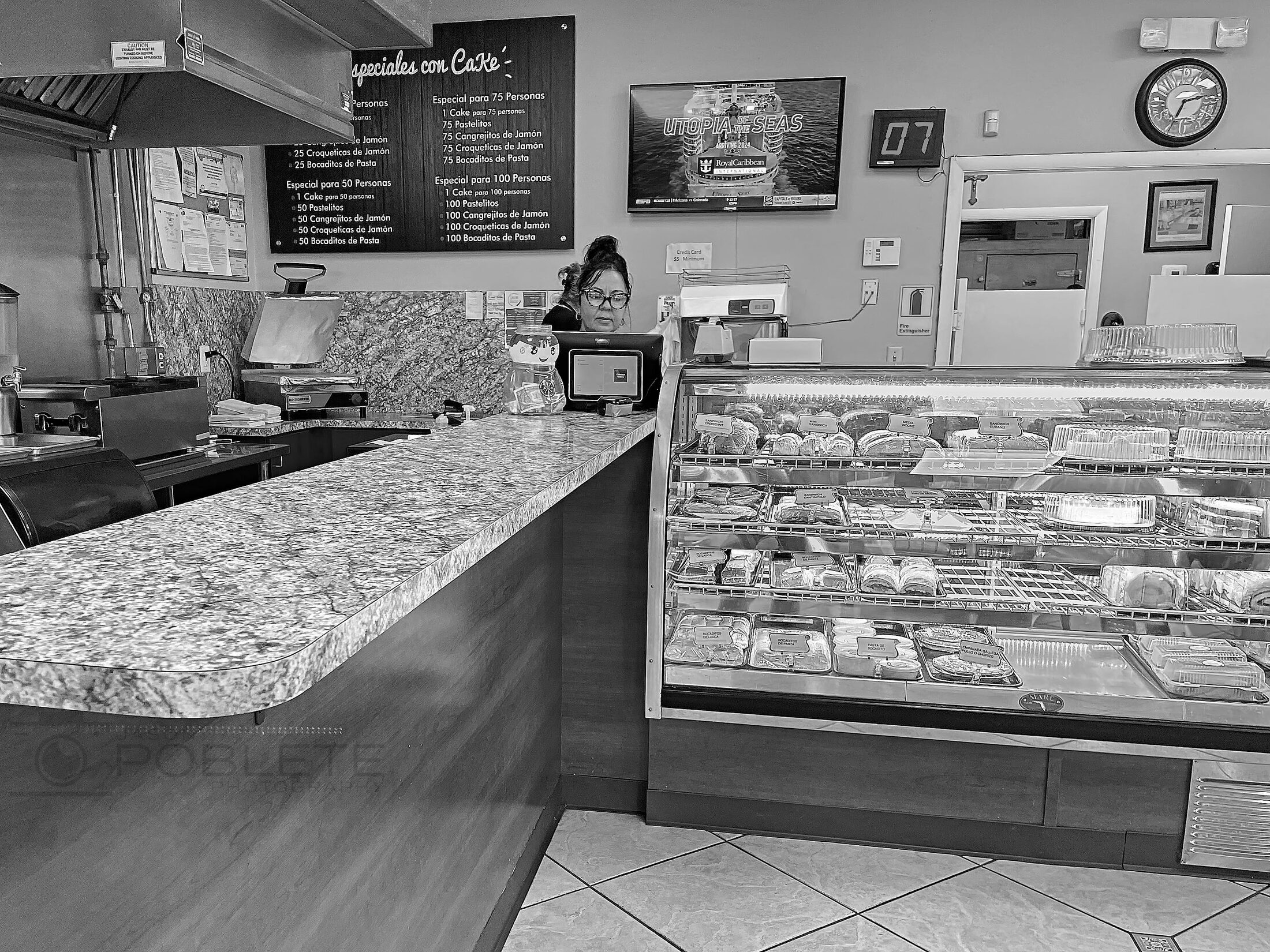 A bakery employee stands behind a long counter and filled pastry case.