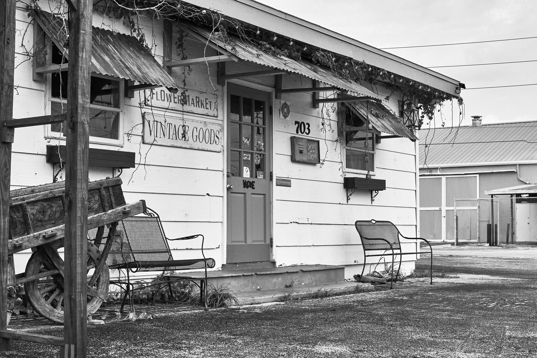 Empty chairs sit outside a weathered flower market and vintage goods shop.