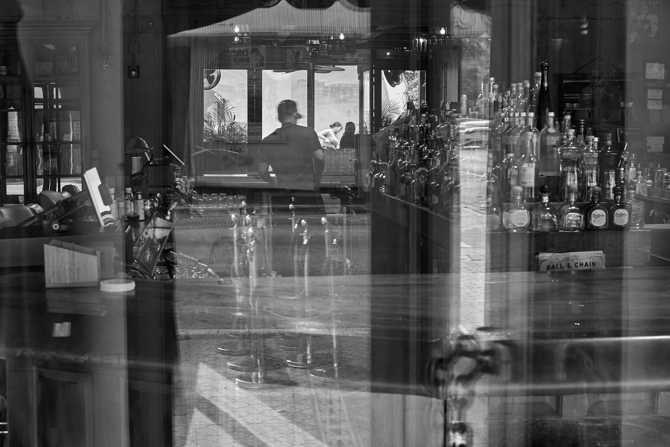 A quiet bar interior is layered with reflections from the street.