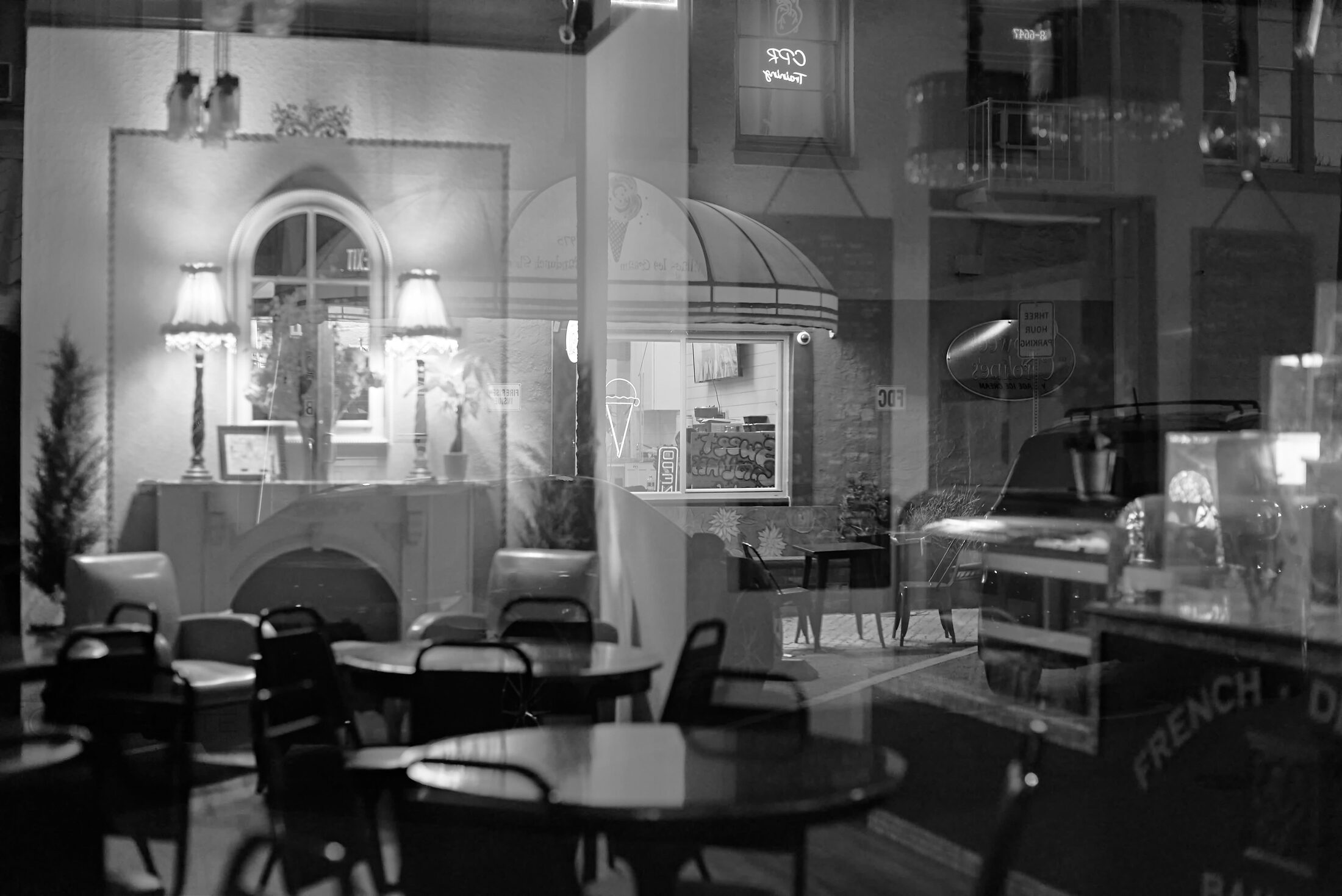 An empty café interior is layered with nighttime storefront reflections.