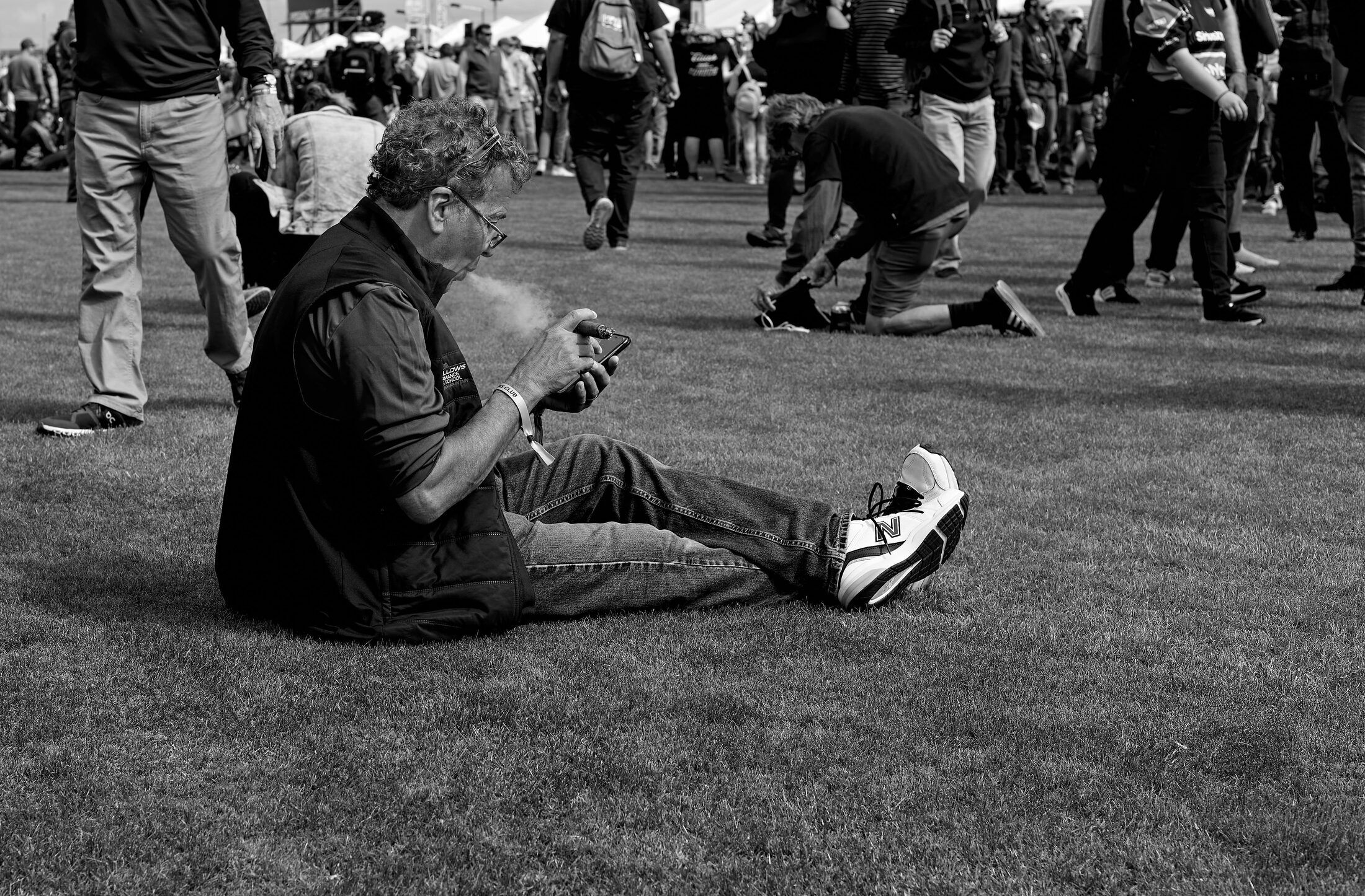 A seated person rests on grass while a crowd gathers in the background.