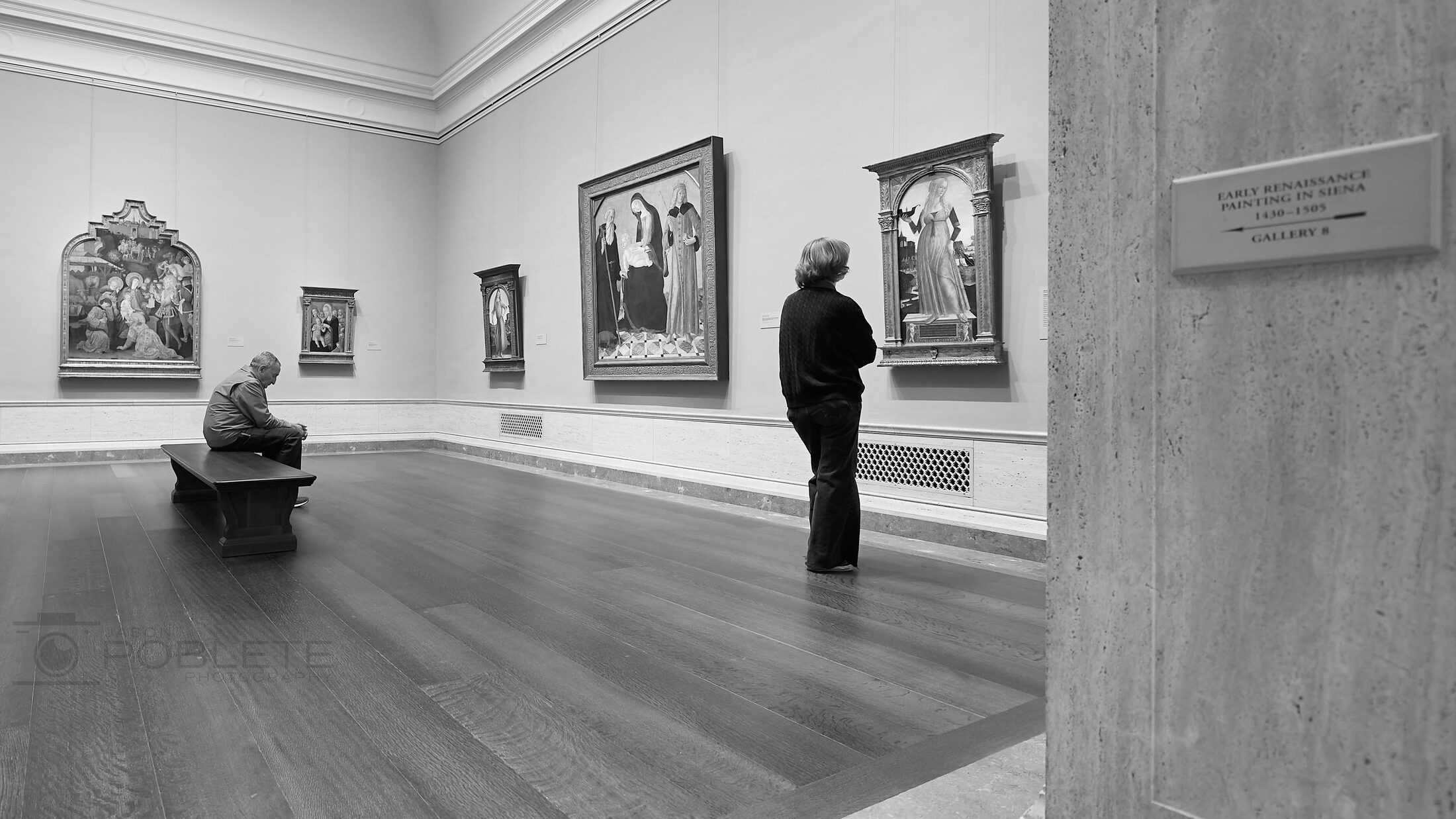Two visitors stand apart in a spacious art gallery.