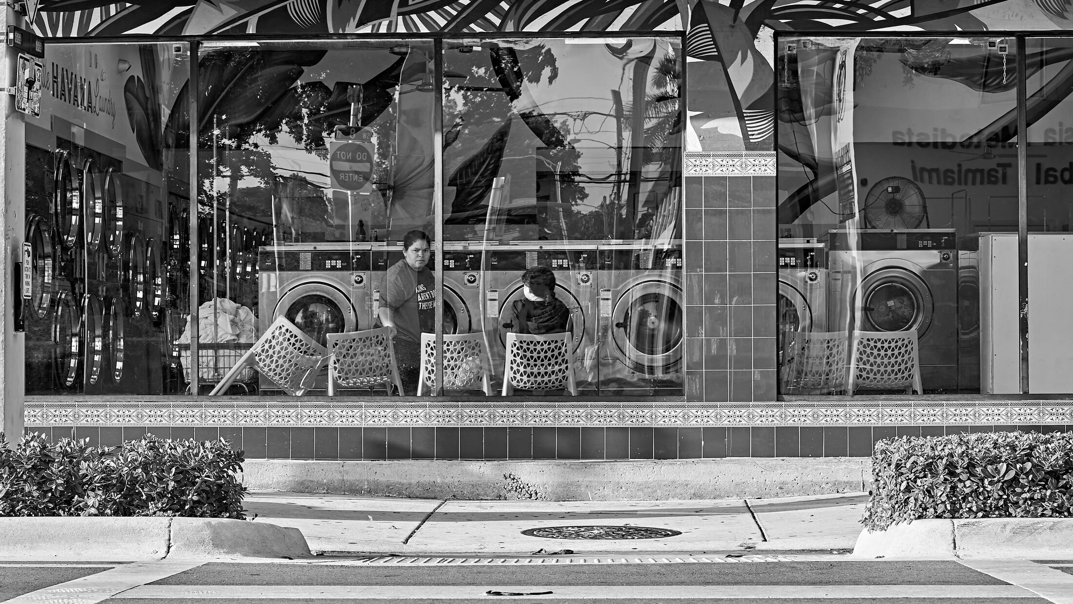 People wait and talk behind a metal railing in a public plaza.