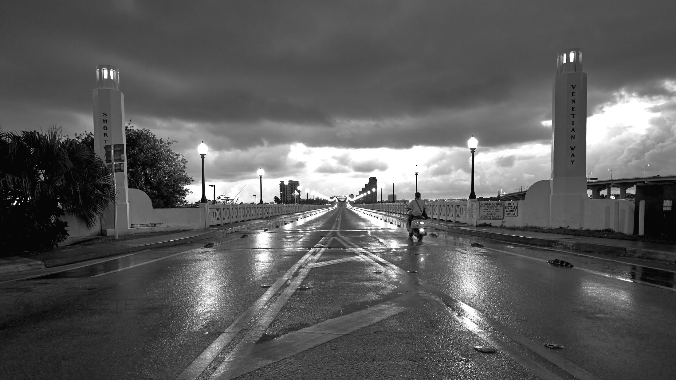 Wet pavement reflects a brightly lit roadside complex under storm clouds.