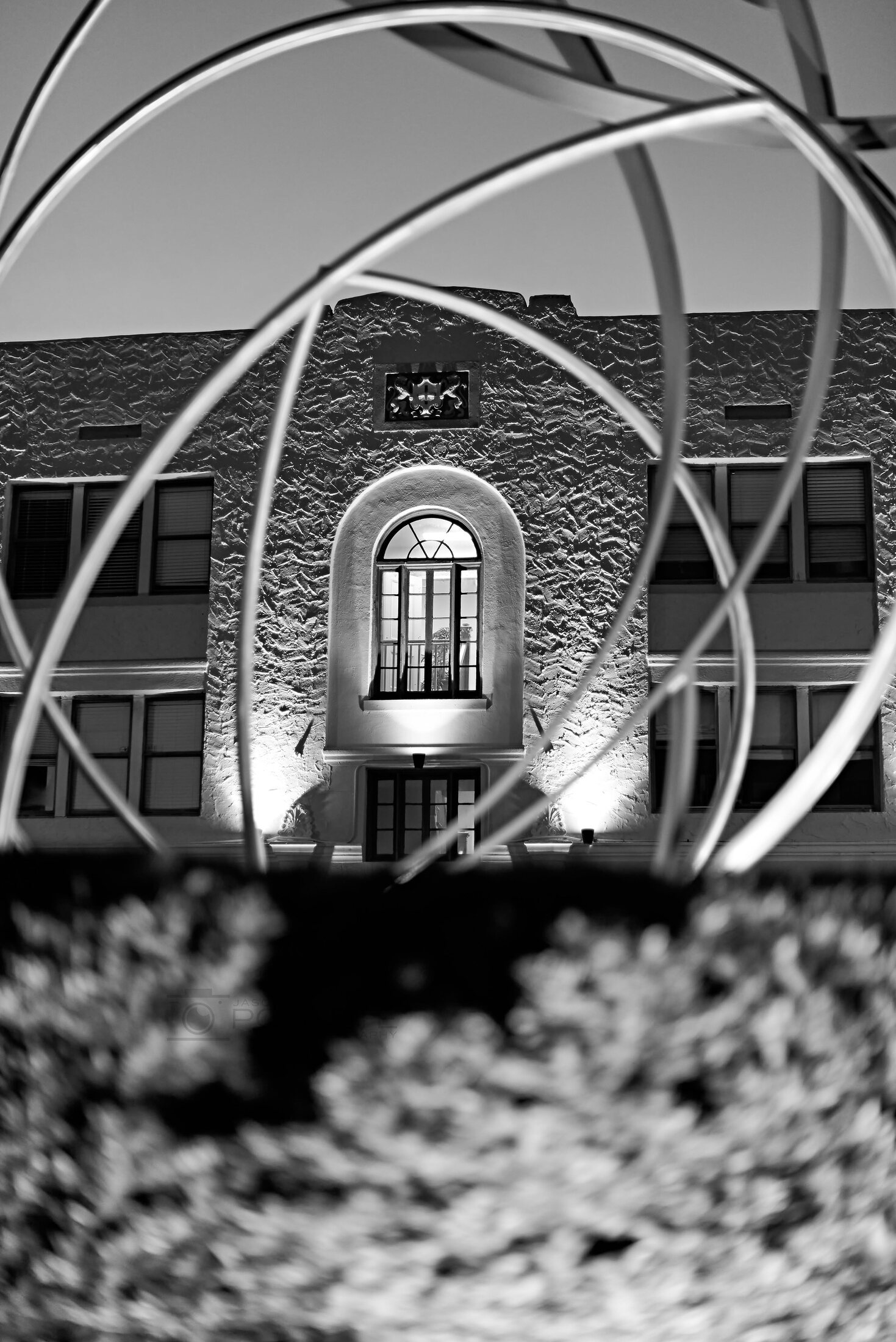 Curving metal bands frame the illuminated arched window of a textured building at night.