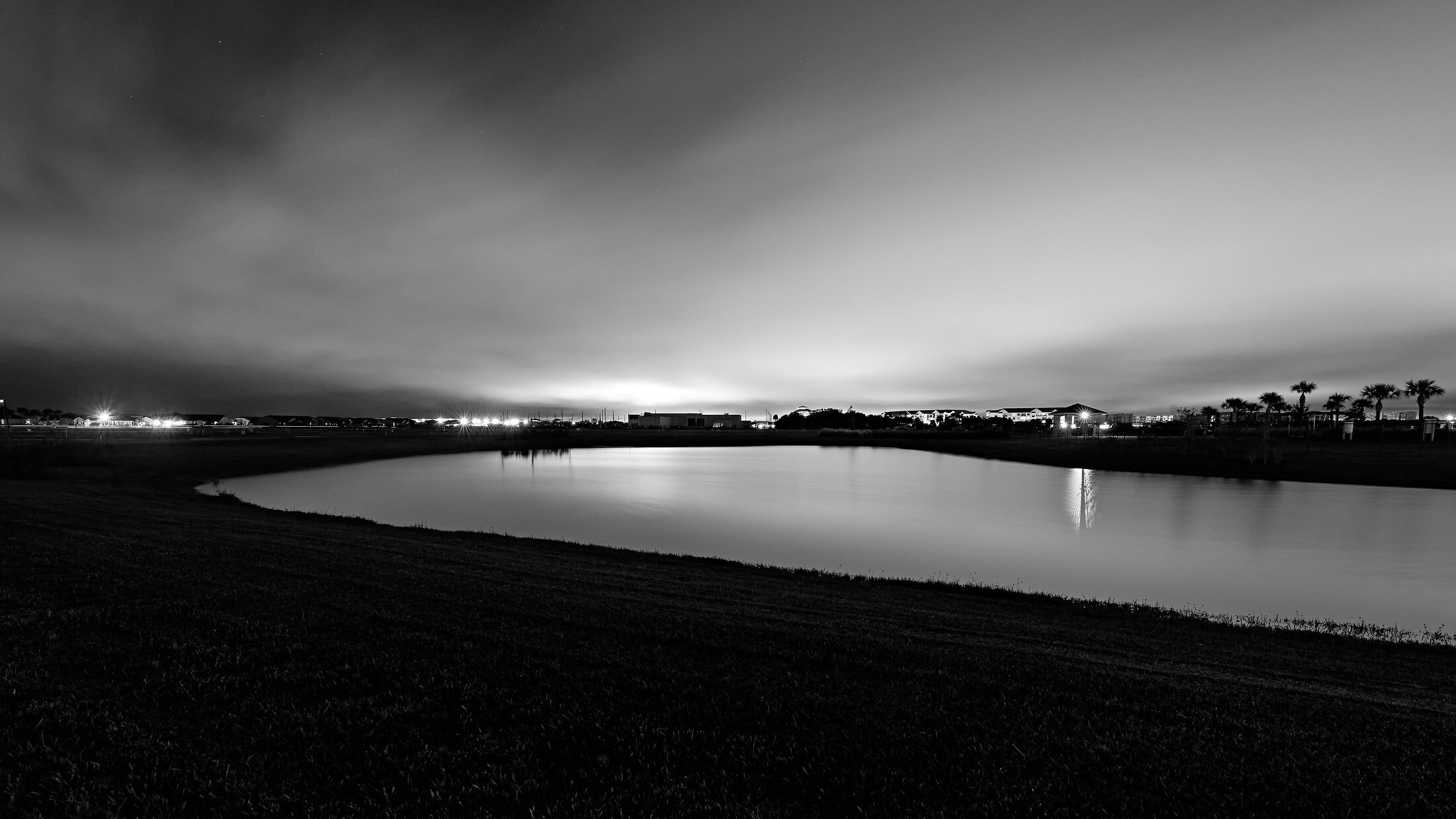 A dark retention pond reflects distant lights beneath a low, glowing night sky.