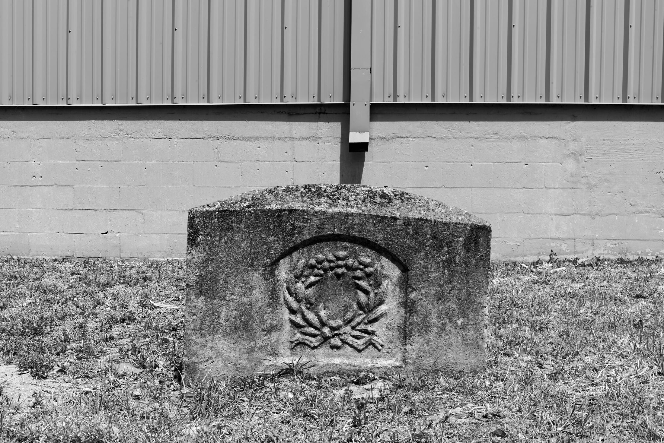 A small weathered grave marker rests beside an industrial wall.