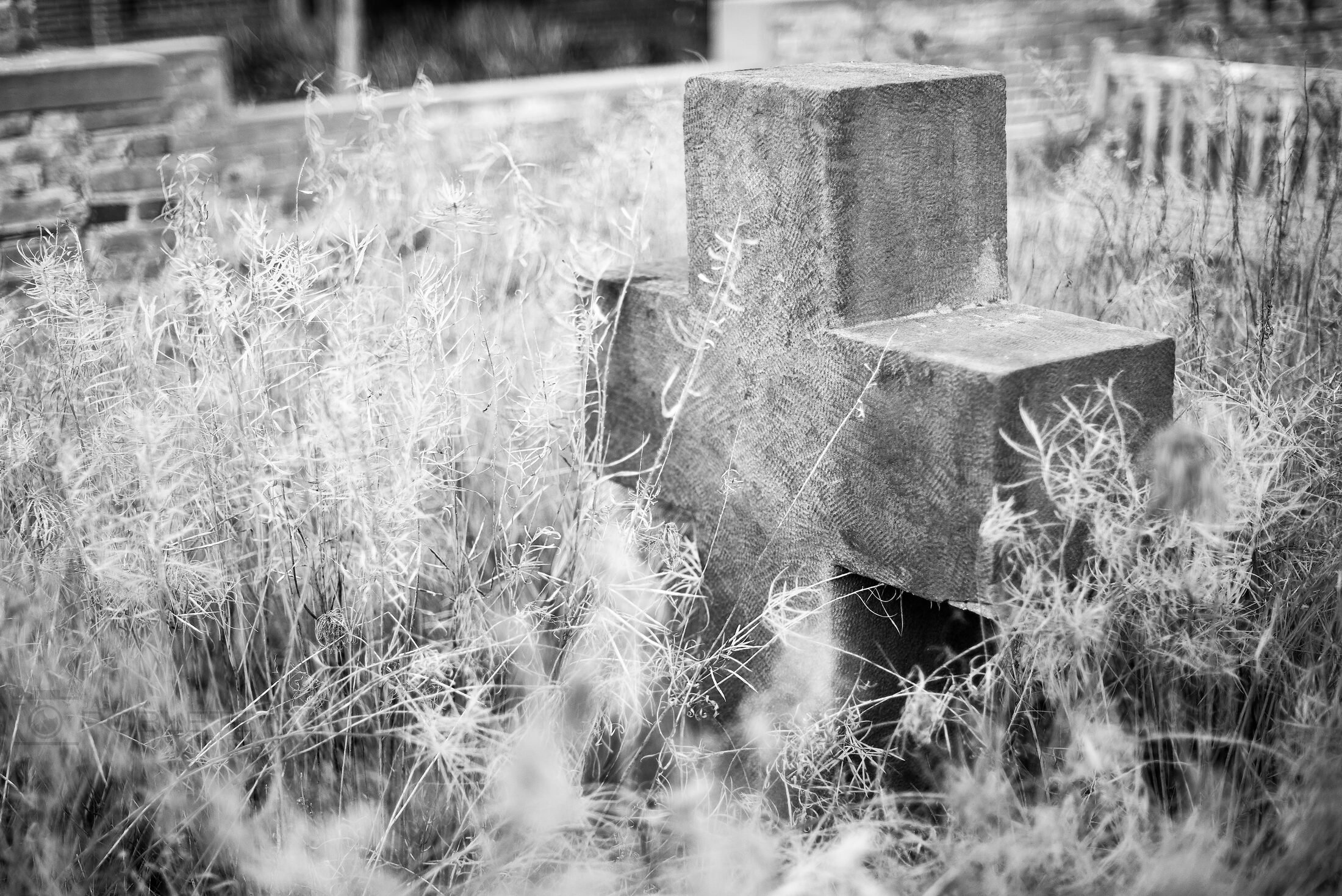 A rough stone cross is partly obscured by tall grass.