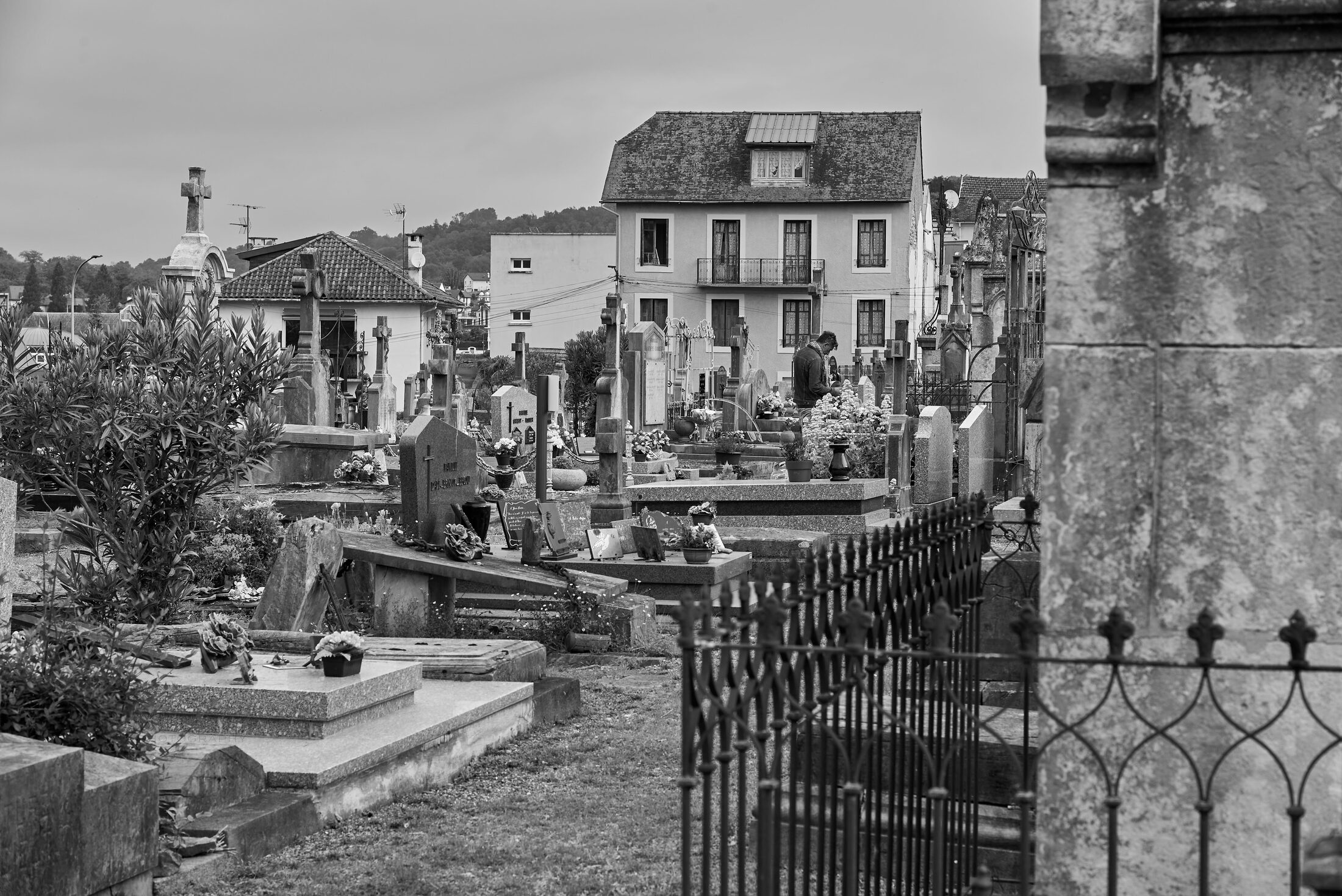 Graves, markers, and iron fencing fill a cemetery bordered by houses.