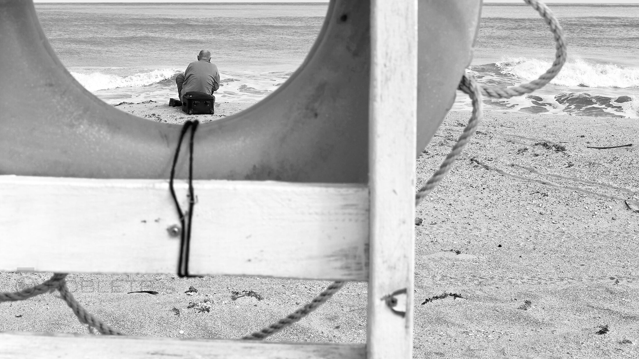 A solitary beachgoer is framed through a curved opening beside the sand.