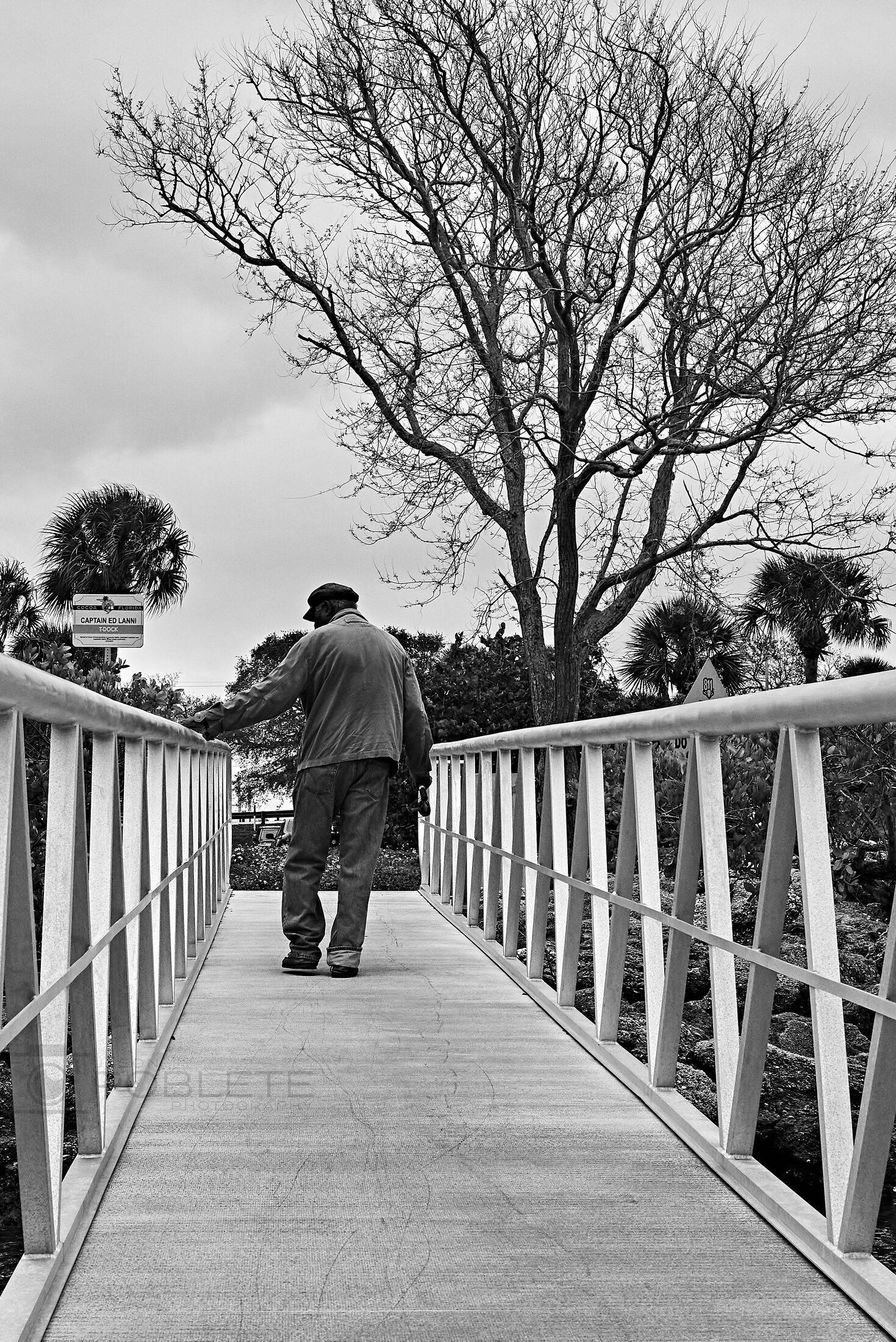 A person carrying fishing gear walks along a pier railing.