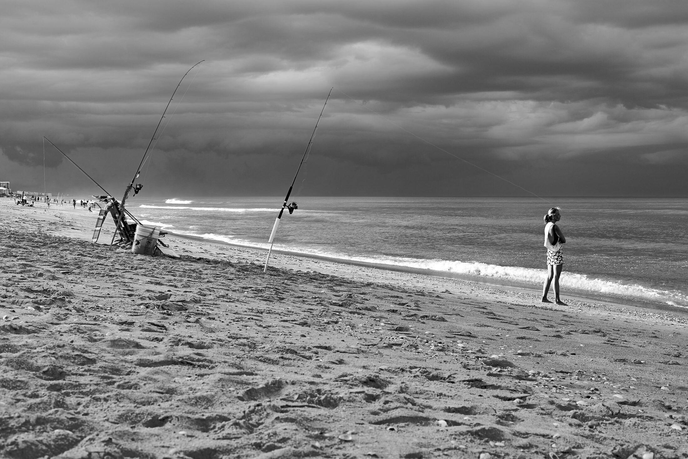 Fishing rods lean toward the surf beneath a stormy sky.