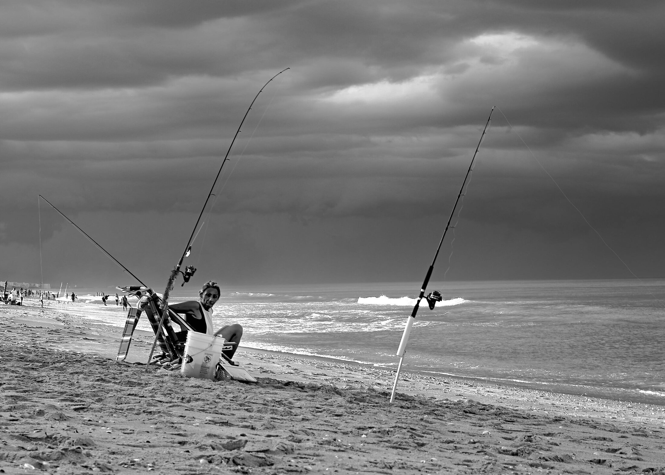 Two anglers tend long fishing rods at the waterline.