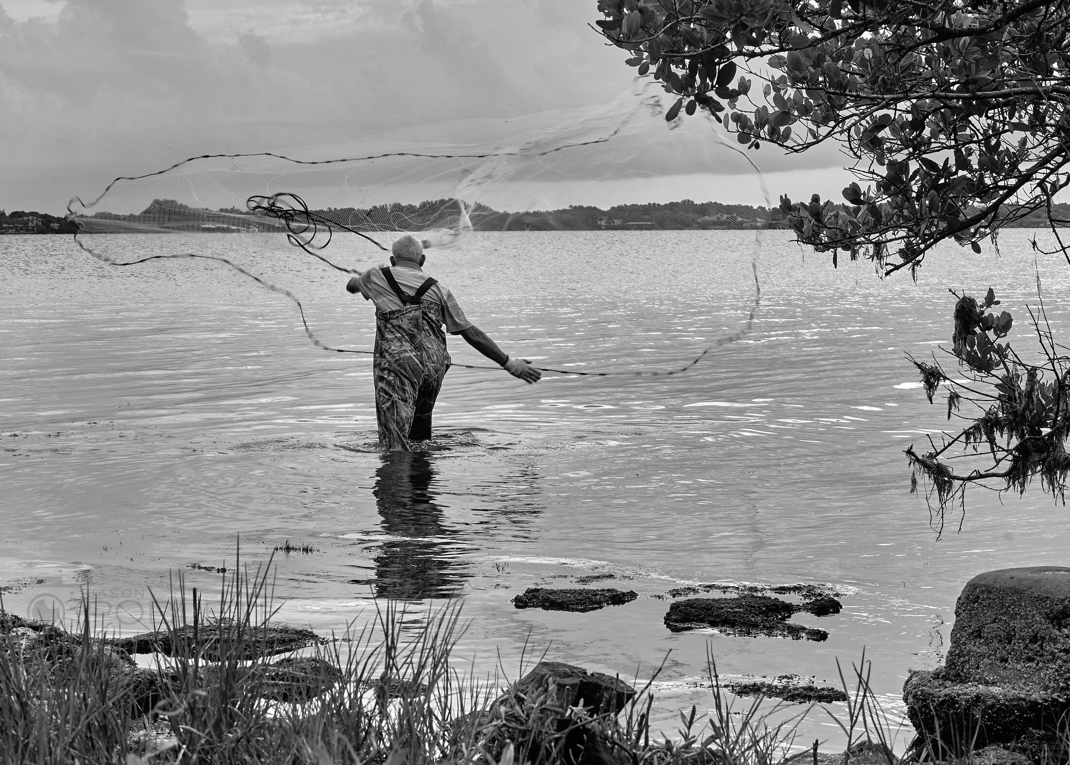 An angler casts a net or line while standing in shallow water.