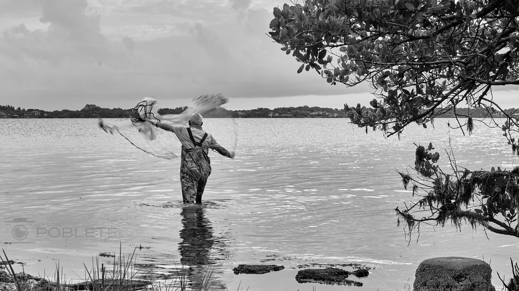 An angler draws back a cast in calm coastal water.