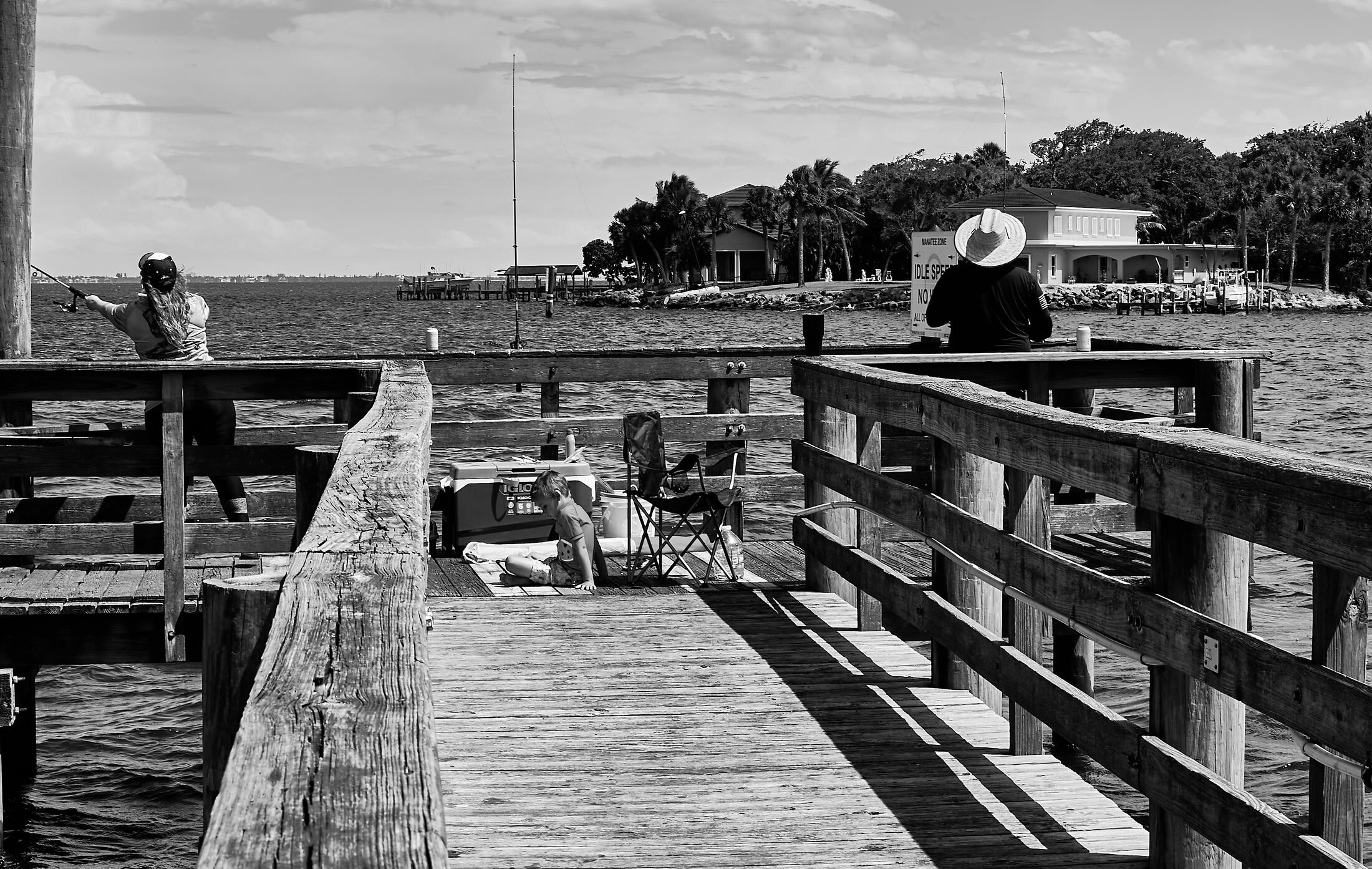 People fish from a long wooden pier beneath an open sky.