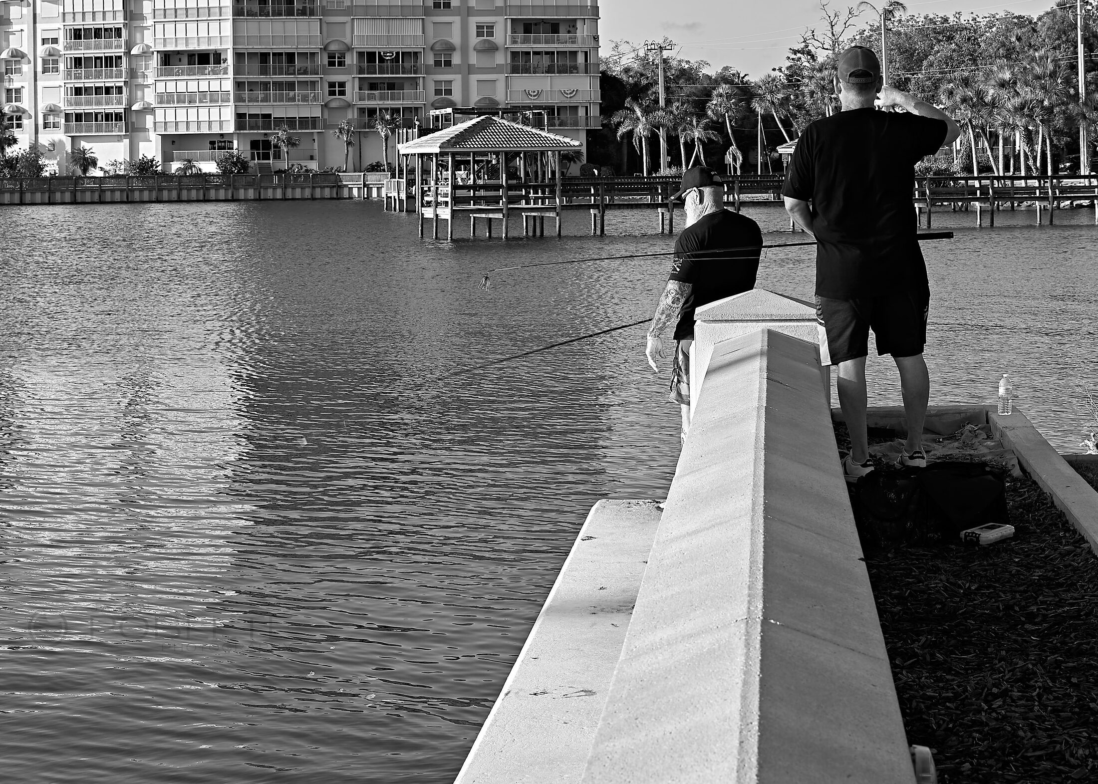 Two people stand at the end of a waterfront railing overlooking a marina.