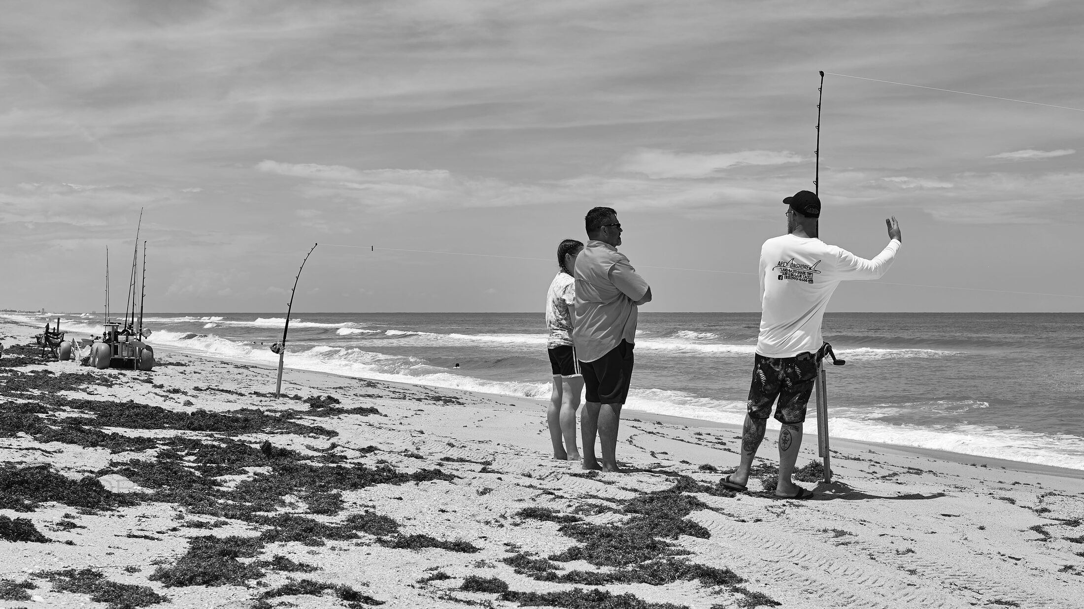 Two anglers stand on a rocky beach with fishing rods raised.