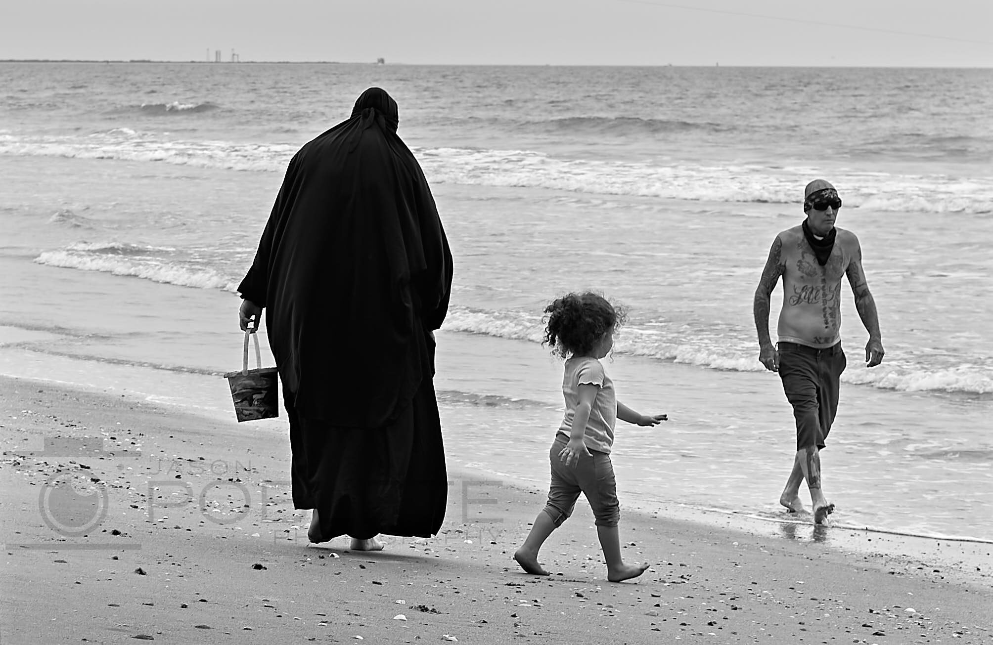 Three people walk along the beach beside a hand-lettered sand sign.