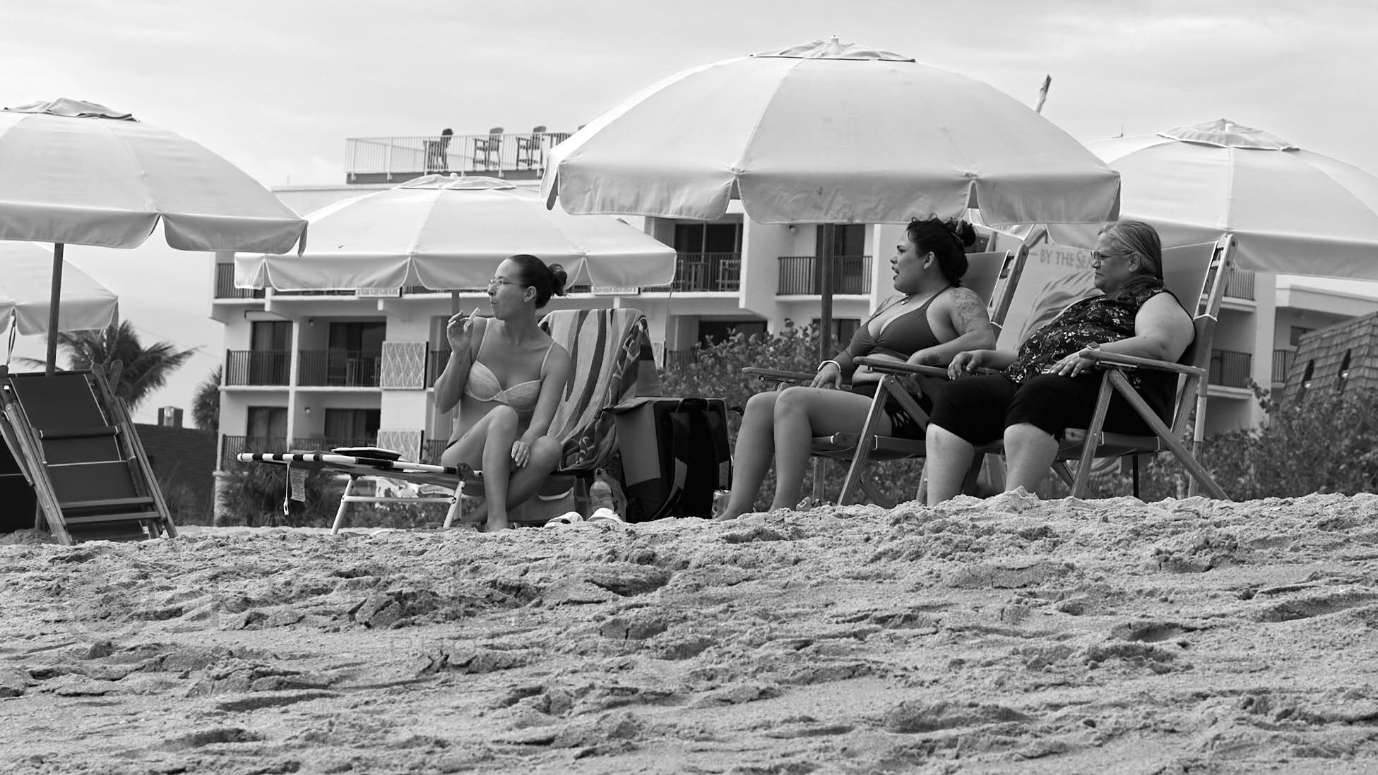 Beachgoers sit beneath umbrellas near weathered waterfront structures.