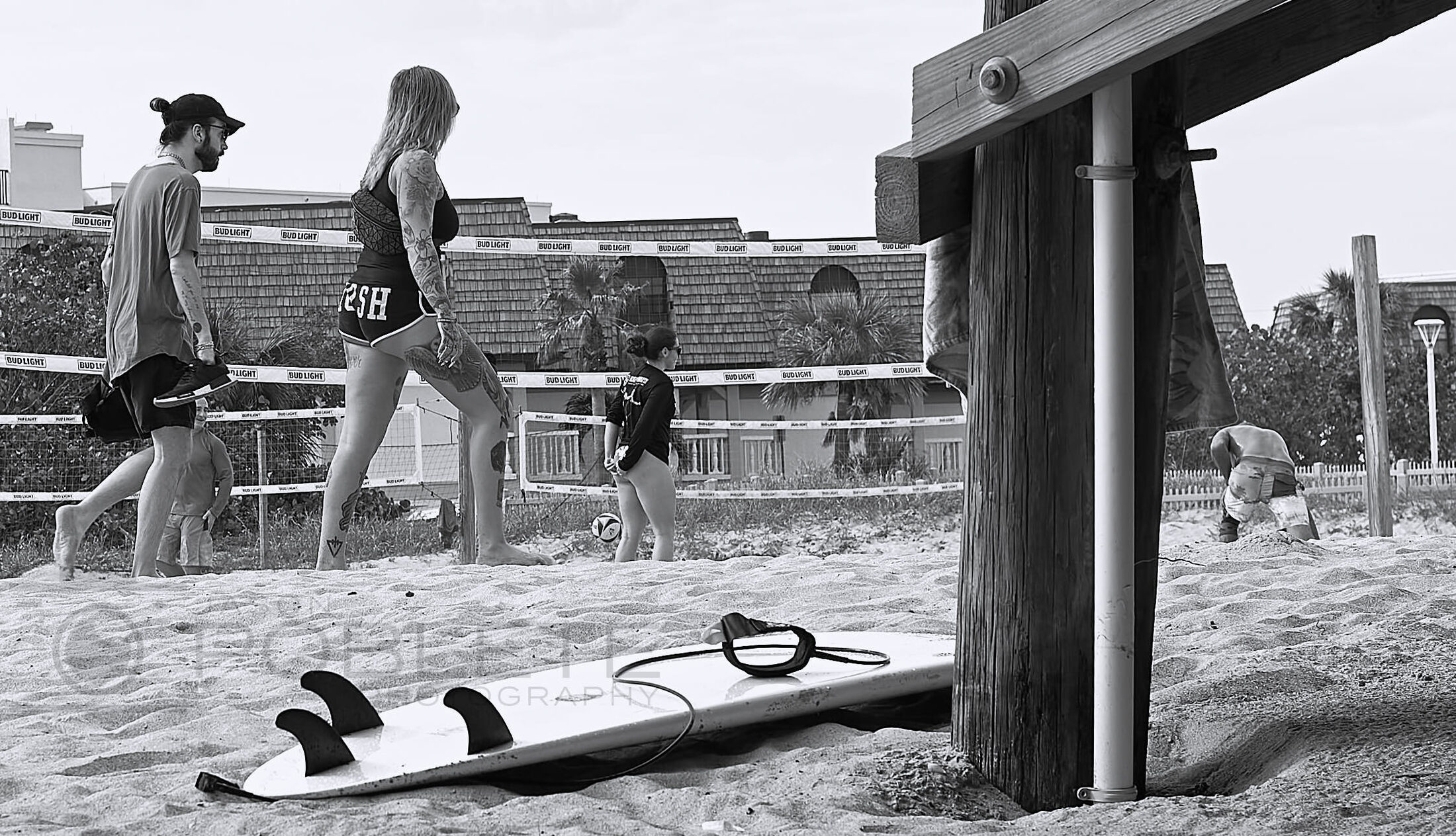 People gather beside surfboards near a beach access pavilion.